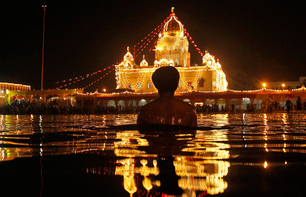 Индус совершает ритуальное окунание на фоне подсвечиваемого храма Бангла Сахиб Сикх в день рождения сикхского гуру Нанак в Нью-Дели (AP Photo/Gurinder Osan)